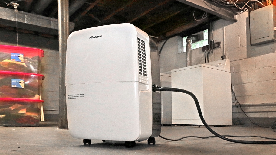 deumidifier sitting on basement floor with storage containers and clothes dryer in background